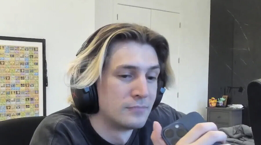 xQc on stream, wearing headphones and looking at a phone